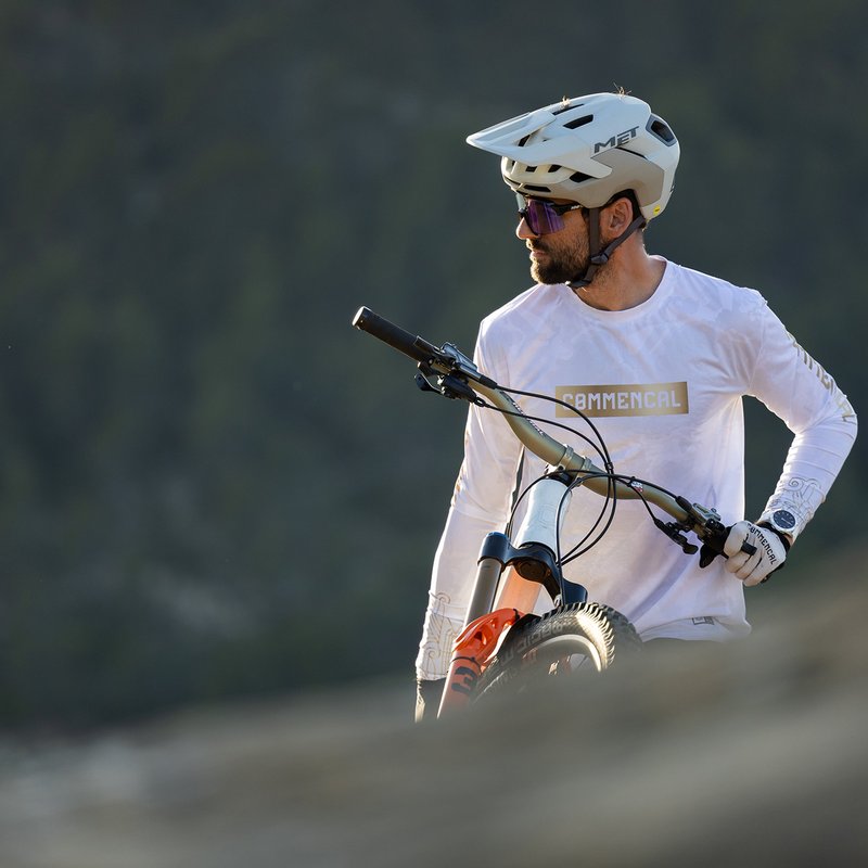 Ciclista de montaña con casco blanco y las gafas 100% S3 puestas, parado junto a su bici en el monte